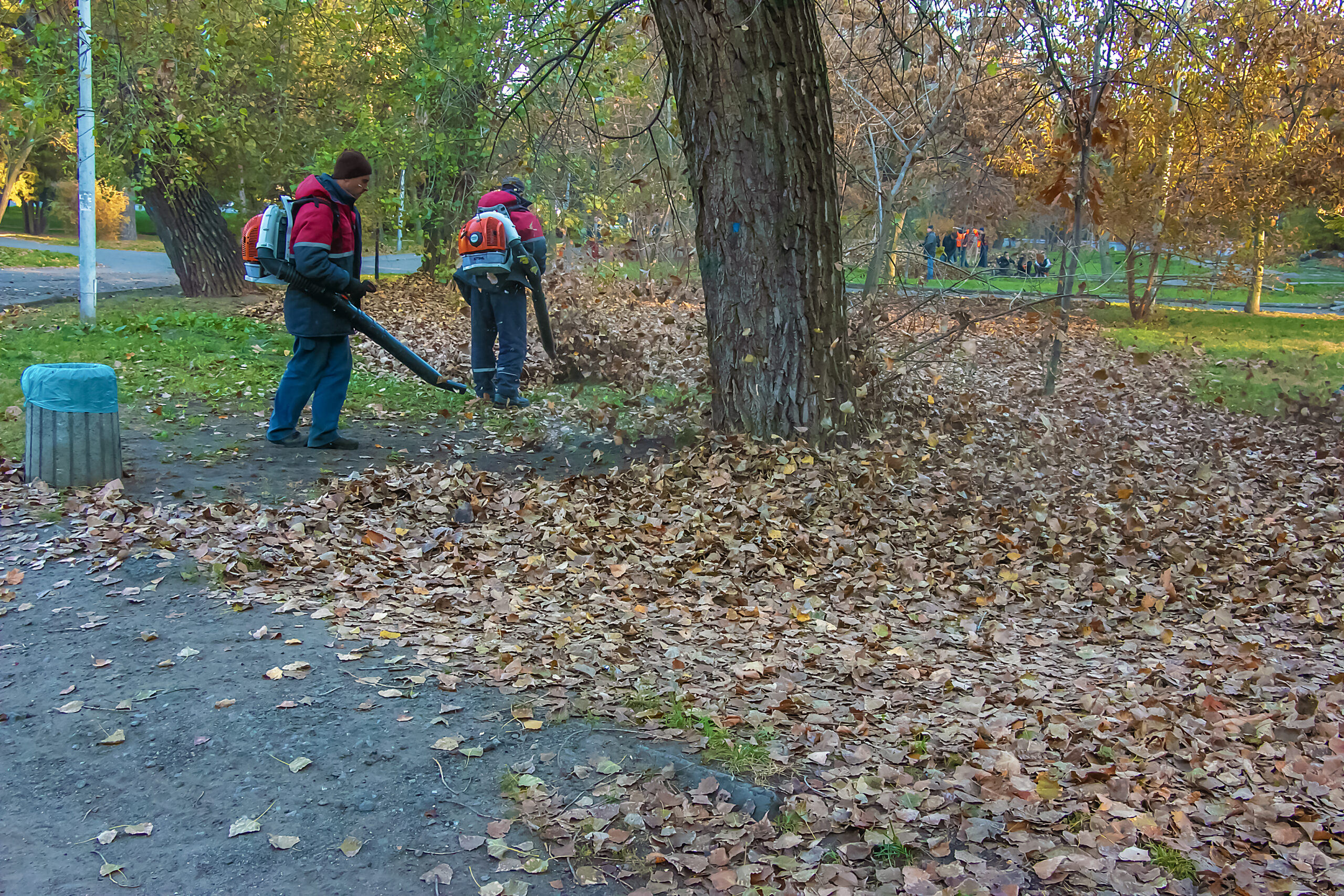 Dnepr, Ukraine - 10.30.2021: Workers at a utility company use a leaf blower to clear fallen leaves from a park alley.